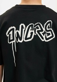 Juodas marškinėliai su ryškiu baltu grafiti stiliaus tekstu "INGRS" ant nugaros. Trumpos rankovės, standartinio kirpimo, pagaminti iš medvilnės.