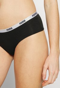 Black cotton brief with a silver elastic waistband featuring 'PUMA' logo printed in black. Smooth texture, minimalistic design.