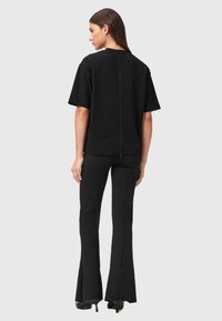 Zwart katoenmix top met een achterrits, korte mouwen, gecombineerd met zwarte flared broek die ritselementen aan de zoom heeft.
