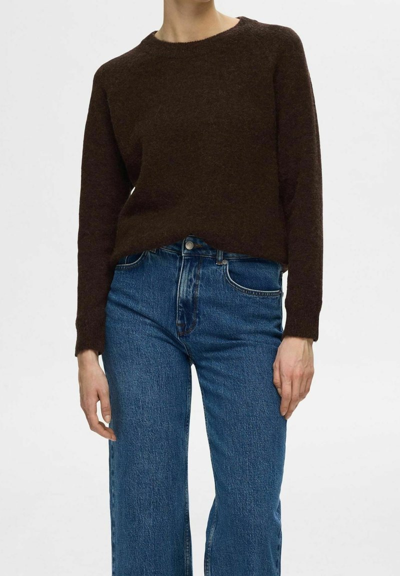Brauner, strukturierter Strickpullover mit rundem Halsausschnitt, langen Ärmeln und einem leicht verkürzten Schnitt, kombiniert mit hellblauen hochwertigen Jeans.