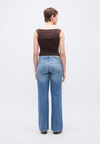 Bruin mouwloos topje en lichtblauwe high-waisted jeans met rechte pijpen, voorzien van een klein logo op het achterkant van de tailleband.