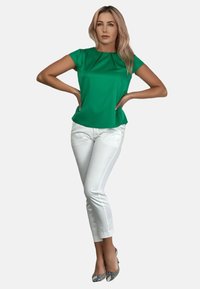 Zielona bluzka z krótkim rękawem z detalami w plisach, połączona z dopasowanymi białymi spodniami i wzorzystymi szpilkami. Gładka tkanina i dopasowany krój.