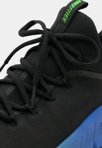 Sort atletiksko med tekstureret overdel, rund tå, flade sorte snørebånd og en blå gradient sål. Grøn "NIKEFREE" branding på hælen.