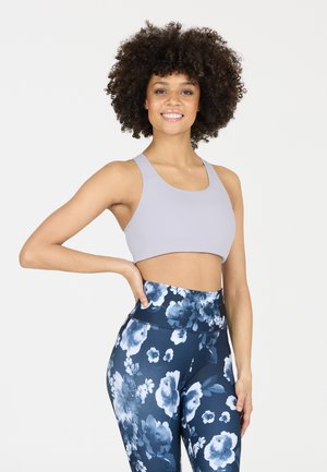 Sujetador deportivo de color gris claro con tirantes anchos, combinado con leggings de cintura alta que presentan un patrón floral oscuro en azul y blanco. Textura suave.