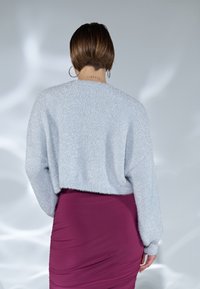 Svetle modrý zkrácený svetr s jemnou texturou, kombinovaný s těsně padnoucími hluboce růžovými sukní. Viditelné švy a dlouhé rukávy.