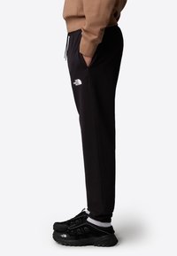 Svarta sweatpants med sidofickor och elastiskt midjeband. Har en vit logotyp på vänstra låret. Kombineras med svarta sportskor.