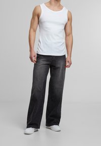 Top de algodón blanco sin mangas con escote amplio, acompañado de unos jeans de mezclilla gris oscuro de corte holgado y zapatillas blancas, presentado sobre un fondo liso.