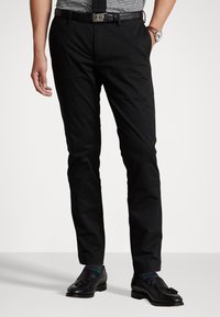 Svarta kostymbyxor med skräddarsydd passform, bältesöglor och en slät yta. I kombination med svarta läderskor och mönstrade strumpor.