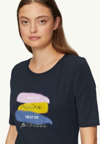 Marineblauwe katoenen t-shirt met korte mouwen; voorzien van meerkleurige tekst in zachte pastelstreken met een mix van lettertypen en stijlen.