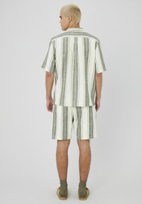 Ensemble de chemise à manches courtes rayée et de shorts dans des teintes blanches et vertes. Tissu texturé avec des rayures verticales et une coupe décontractée.