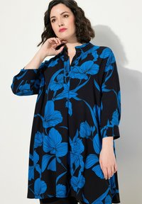 Czarna tunika z niebieskim kwiatowym wzorem, z kołnierzykiem i zapięciem na guziki. Luźny krój z długimi rękawami i zaokrąglonym dołem.