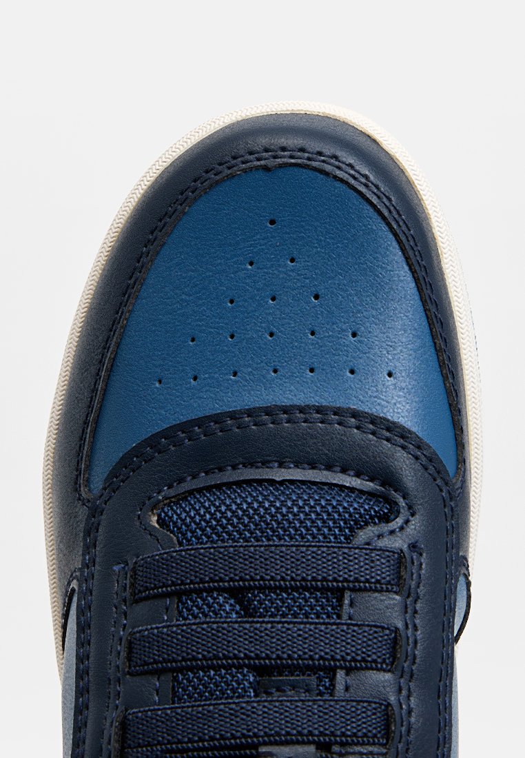 Marineblaue Leder- und TextilSportchuhe mit strukturierten Oberflächen, kreisförmigen Perforationen an der Zehenpartie und flachen Schnürsenkeln. Weiße Gummisohle.