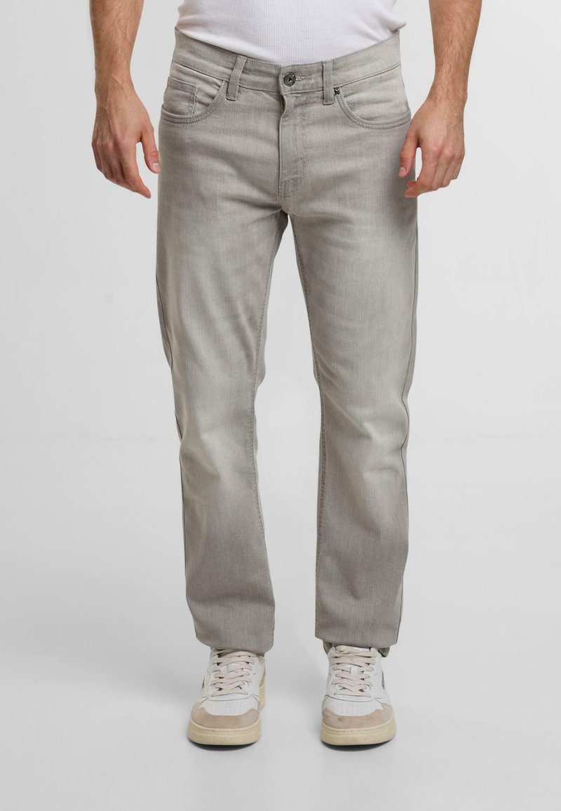 Jeans in denim grigio chiaro con taglio dritto, dotati di tasche anteriori, chiusura con zip e una texture sottile. Abbinati a sneaker bianche.