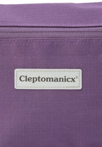 Lila Stofftasche mit einem weißen Etikett, auf dem der Markenname "Cleptomanicx" aufgenäht ist. Reißverschlussdetail oben sichtbar.
