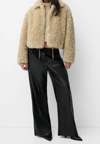 Faux fur beige jakke med en cropped design, parret med højtaljede sorte satinbukser med elastisk talje og snor.