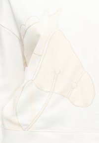 Περίγραμμα της κεφαλής ενός αλόγου με λεπτομέρειες ανεμούρας ραμμένες σε λευκό ύφασμα, που δείχνει υφή και διακριτική σκίαση.