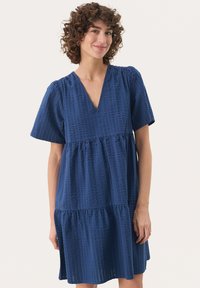 Mörkblå klänning med korta ärmar, V-ringning, lager-kjol och textil med en subtil rutig mönstring.