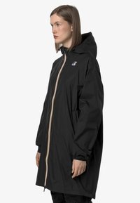 Veste imperméable noire avec capuche, dotée d'une fermeture éclair colorée et de poignets élastiques, conçue avec une coupe ample et des poches latérales.