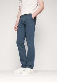 Blå bomullsbyxor med rak passform, sidofickor och subtila sömnadsdetaljer, i kombination med vita sneakers.