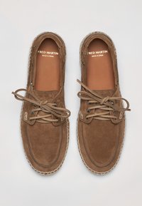 Chaussures en suède marron à lacets légers, avec un bout arrondi et des coutures blanches autour de la semelle. Nom de la marque visible à l'intérieur.