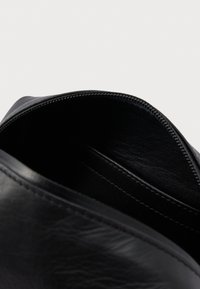 Czarna skórzana saszetka na zamek z otwartą górą, pokazująca gładką podszewkę i przeszycia wewnątrz.