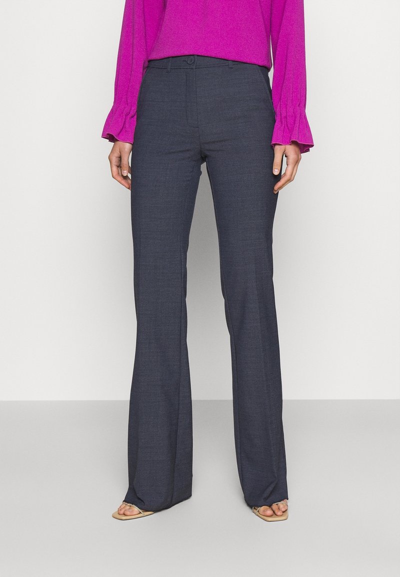 Personne portant un pantalon ample gris foncé, un haut rose vif à manches longues avec des manches volantées, et des sandales beiges ouvertes à l'avant.