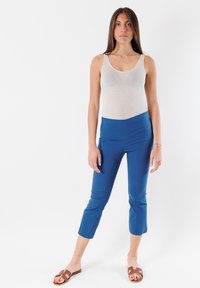 Canotta grigia chiaro aderente abbinata a pantaloni blu a metà polpaccio. I pantaloni hanno una texture liscia e un design aderente, con cuciture in rilievo e una vita sagomata.