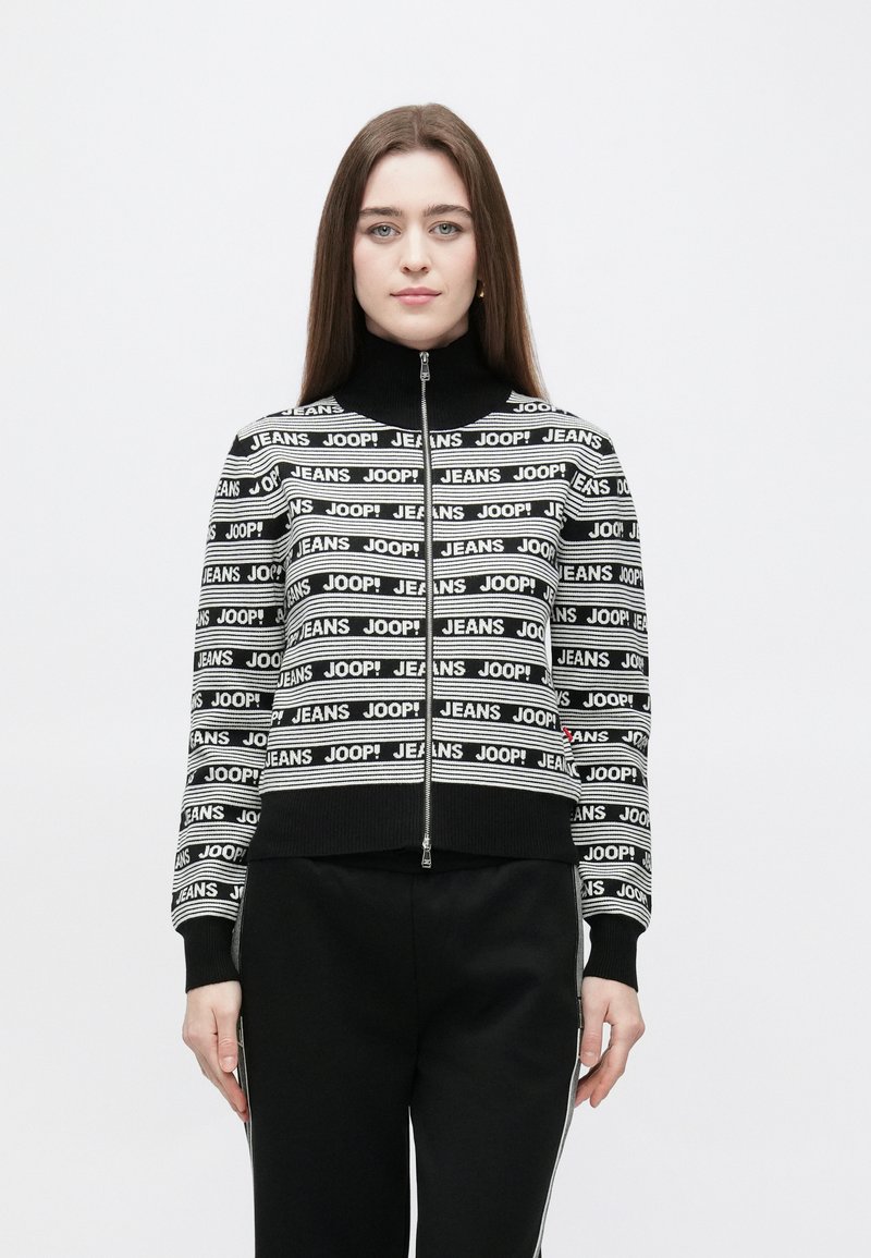 Black and white cropped sweater with zip, featuring striped pattern and "JEANS JOOP!" text. High collar and ribbed cuffs, made from soft material.