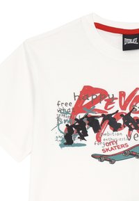 T-shirt bianco in cotone con stampa grafica multicolore contenente testo e silhouette di skateboarder. Collo rotondo con bordino rosso a contrasto.