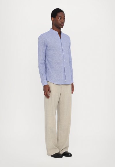 Camicia a maniche lunghe azzurra chiara con colletto a band, tessuto texture e chiusura frontale con bottoni, abbinata a pantaloni beige a gamba larga e scarpe nere.