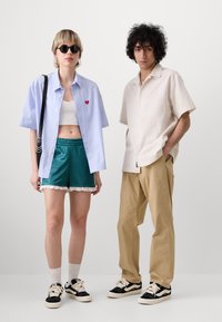 Lyseblå kortermet skjorte med rødt hjerte, hvit crop topp, turkise shorts med blonder, beige kortermet skjorte, khakibukser, sorte joggesko.