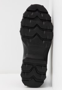 Semelle de botte noire robuste avec des rainures profondes et des motifs conçus pour l'adhérence et la durabilité.