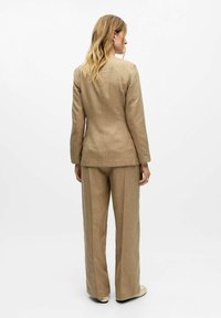 Beige maßgeschneiderter Anzug bestehend aus einem taillierten Blazer und weit geschnittenen Hosen, gefertigt aus strukturiertem Stoff mit vertikalen Streifen, von hinten betrachtet.