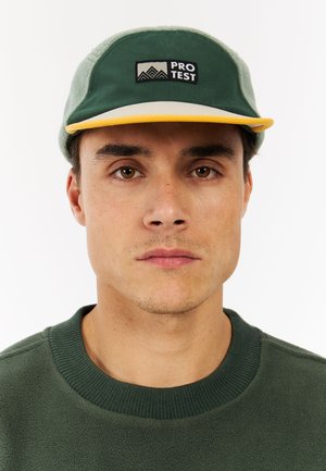 Green cap with a yellow brim, featuring a black "PRO TEST" logo, soft texture, and a structured design. Worn with a green fleece sweater.