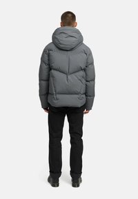 Padded gray puffer jacket s kapucňou, s prešívaným dizajnom a elastickými manžetami, v kombinácii s čiernymi nohavicami a čižmami.