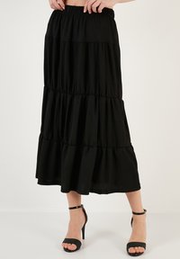 Black, tiered maxi skirt featuring an elastic waistband, lightweight fabric, and a flowy silhouette, paired with black strappy high heels.