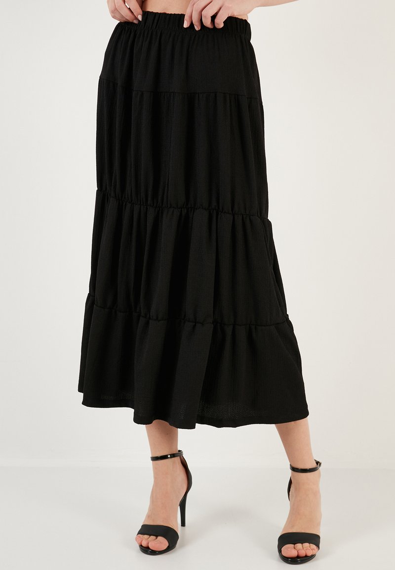 Black, tiered maxi skirt featuring an elastic waistband, lightweight fabric, and a flowy silhouette, paired with black strappy high heels.