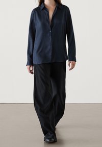 Camicia a maniche lunghe blu navy con bottoni frontali e colletto, abbinata a pantaloni neri larghi. Tessuto liscio, vestibilità comoda e dettagli minimi.