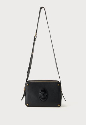 Sac bandoulière en cuir noir avec sangle réglable, fermeture éclair dorée, clous d'angle dorés et emblème tête de Méduse noir sur le devant.