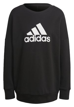 Zwarte sweatshirt met witte "adidas" logo, gecombineerd met grijze taps toelopende broek met drie verticale strepen en zwarte sportschoenen.