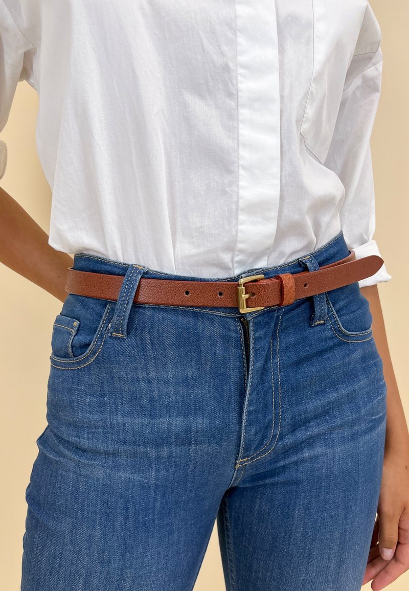 Personne portant un jean bleu et une chemise blanche rentrée, avec une ceinture en cuir marron attachée à la taille.