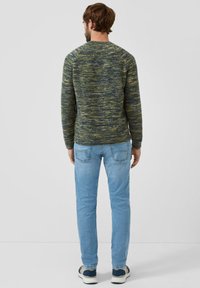 Wiązany sweter w ciemnozielonym i niebieskim melanżowym wzorze, z okrągłym dekoltem, dopasowany fason. Noszony z jasnoniebieskimi dżinsami i codziennymi trampkami.