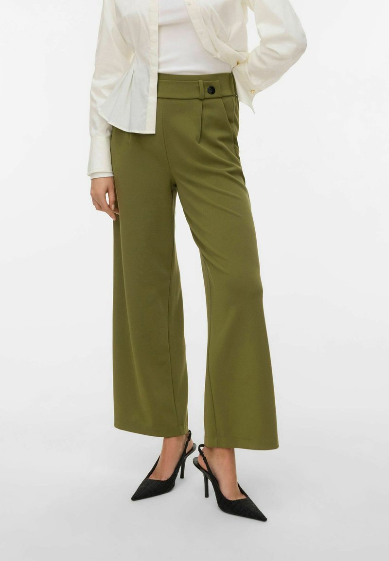 Pantalon large kaki taille haute avec une fermeture à un bouton et des poches latérales, associé à des chaussures à talons noires à bride arrière.