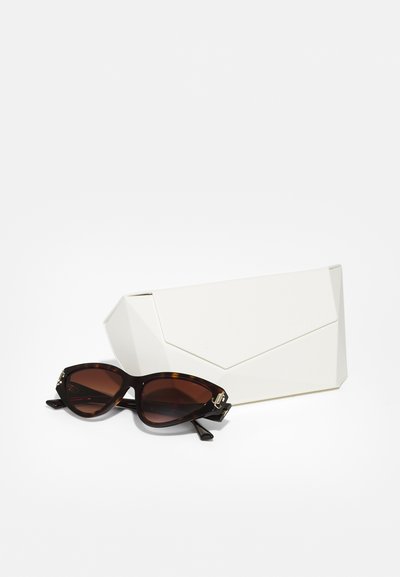 Des lunettes de soleil en écaille de tortue brune avec une large monture angulaire sont posées à côté d'un étui géométrique blanc. Les deux articles présentent des lignes épurées et aucun motif visible.