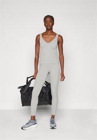 Gry ribbetid trenings tank top og leggings kombinert med grå sneakers, holder en svart treningsbag. Enkel design, tettsittende silhuett.