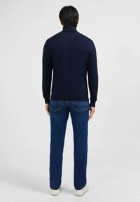 Pull à col roulé navy avec manches longues, poignets et ourlet côtelés. Associé à un jean bleu et des baskets blanches. Texture lisse, design simple.