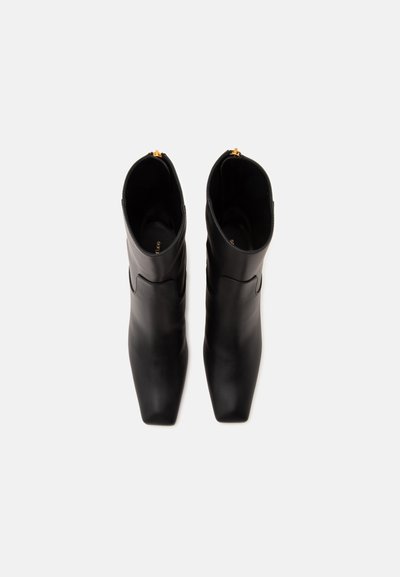 Paire de bottes en cuir noir mi-mollet à bouts carrés avec tirettes de fermeture éclair dorées, vues de dessus sur fond blanc.