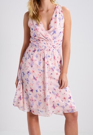 Bezrękawna jasnoróżowa sukienka z kolorowym nadrukiem motyli, dekoltem w serek i marszczoną talią, noszona przez stojącą kobietę.