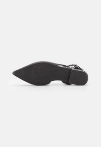 Zapato negro de punta afilada con textura suave, tacón bajo en bloque y correa al tobillo con detalle de hebilla plateada. Suela de goma.