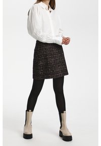 Vit skjorta med puffärmar, parat med en strukturerad mörk kjol. Modellen har på sig ogenomskinliga svarta strumpbyxor och beige ankelstövlar med tjocka svarta sulor.